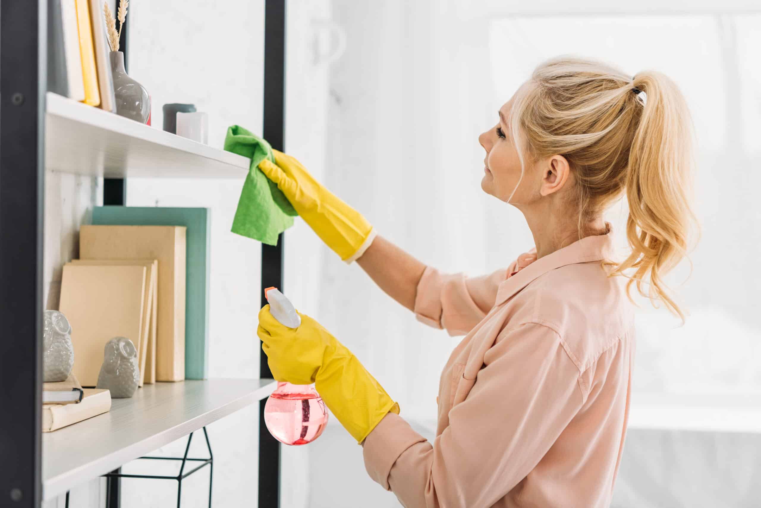 Senior woman with pony tail cleaning shelves with rag